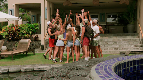 Peter Cipriano, Braeden Holliday, Scarlett Bentley, Shyanne Blankenship, Kaylee Needham, Bradley Bobbit, and Clint Smith in summer clothes stand in a circle with raised hands outside a modern villa, surrounded by greenery, lounge chairs, and a pool.