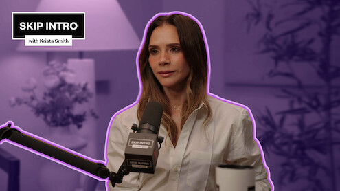 Victoria Beckham in a white shirt speaks into a microphone during a podcast interview, sitting in a softly lit studio with plants and a lamp, mood is calm and focused, overlay text reads "Skip Intro with Krista Smith".