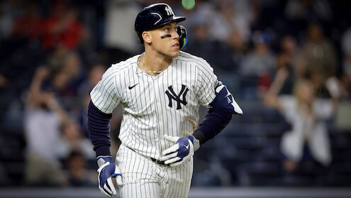 New York Yankees baseball player in pinstripe uniform runs on field during a night game; blurred crowd in the background creates an energetic, competitive atmosphere.