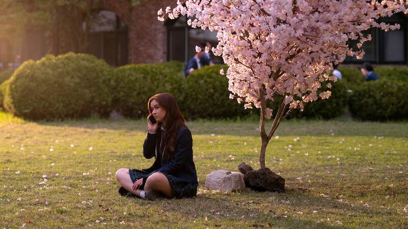 Anna Cathcart as Kitty Song Covey sits under a tree with pink blossoms in Season 2 of 'XO, Kitty' 