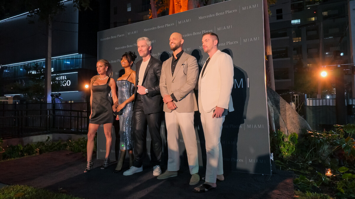 Five well-dressed people posing together on an outdoor evening event stage, city buildings and greenery in the background, creating a formal and celebratory mood.