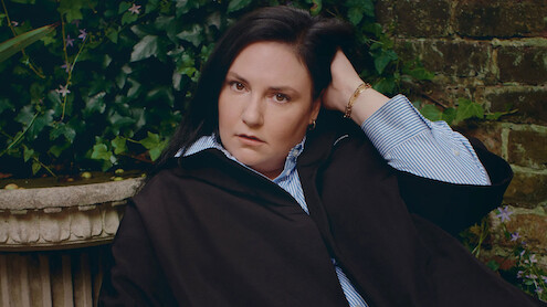 Headshot of Lena Dunham against a brick wall.