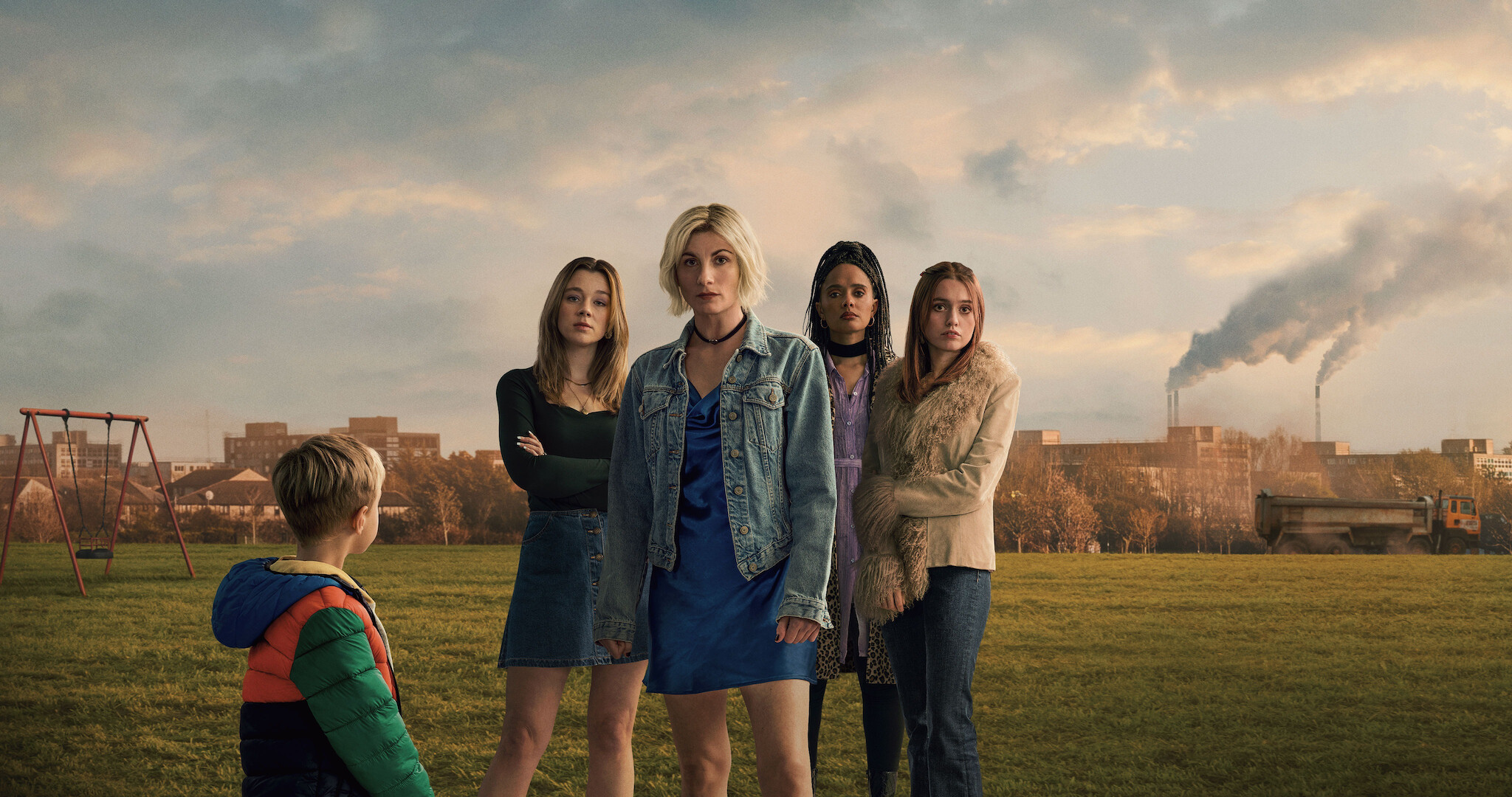 Toxic Town key art - four women standing in a field face the camera while a young boy looks up at them. 