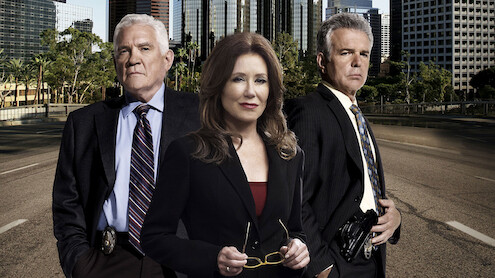 Three serious-looking detectives in suits stand on an empty city street with tall buildings and trees in the background, suggesting an urban law enforcement setting.