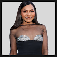 Mulher usando um vestido preto com parte de cima transparente e detalhes brilhantes, de pé, em frente a um fundo cinza-claro, sorrindo e fazendo pose para a câmera.