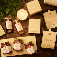 A cozy, warm-toned flat lay of assorted elegantly-packaged gift items, including candles, jars, boxes, and honey, arranged on a wooden table with pine branches, evoking a festive and inviting holiday mood.