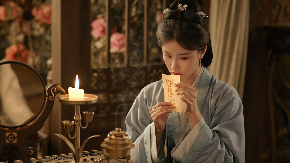 Uma mulher chinesa segura um papel amarelado com uma escritura próximo à sua boca, em uma sala à meia luz e com decoração antiga