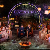 A group of well-dressed people sit in a semi-circle outdoors at night, under lanterns and trees, with a neon "Love Is Blind" sign behind them, creating a festive, lively, and glamorous TV show reunion atmosphere.