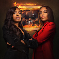 Duas mulheres estão de pé, com ar confiante, diante de um retrato de família em chamas, usando ternos, um escuro e o outro vermelho, em um cenário dramático. Com expressões intensas e os braços cruzados, elas transmitem uma sensação de tensão e conflito.