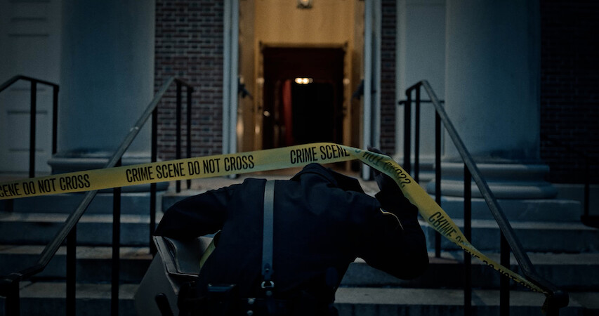 A police officer pulls up crime scene tape.