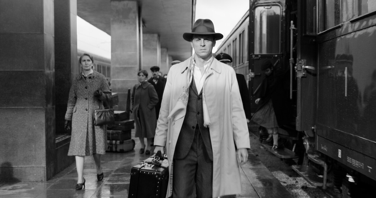 Black and white photo of Andrew Scott as Tom Ripley walking through a train station in 'Ripley'