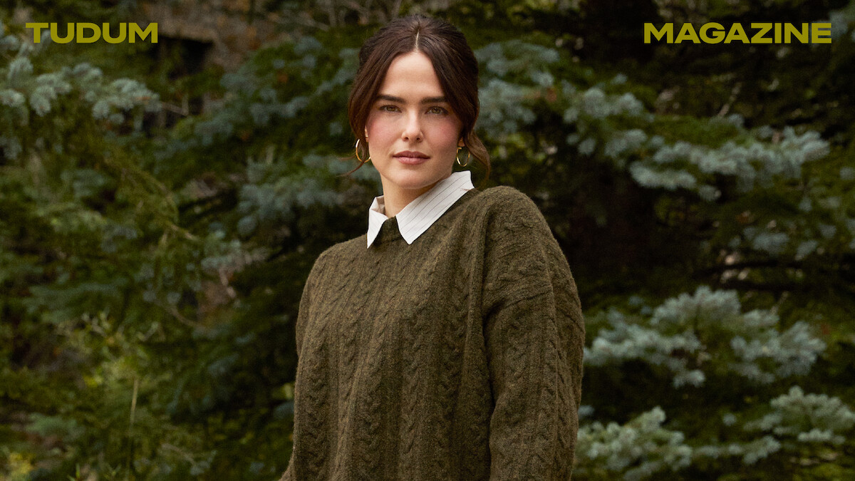 Zoey Deutch stands against a backdrop of trees