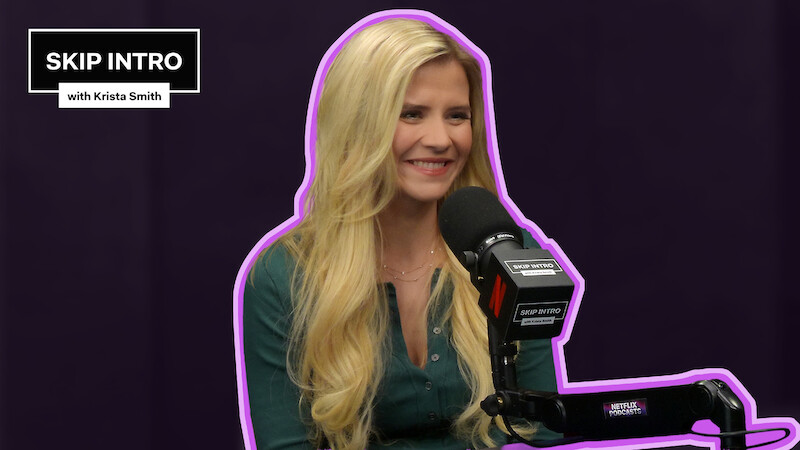 Elizabeth Smart sits smiling in front of a microphone during a podcast recording for "Skip Intro with Krista Smith." The background is purple, and the podcast logo appears in the top left corner.