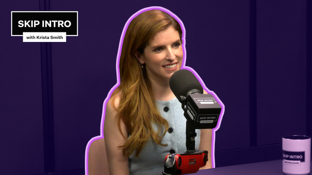 Anna Kendrick, smiling in front of a microphone labeled "SKIP INTRO." She wears a sleeveless, light blue top. The background is deep purple with a purple outline around her.