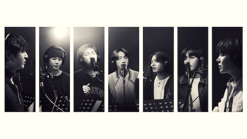 Seven people in a recording studio, each standing at a microphone with music stands, singing or speaking, black and white, portrait orientation, individual spotlight on each person, professional, creative environment.