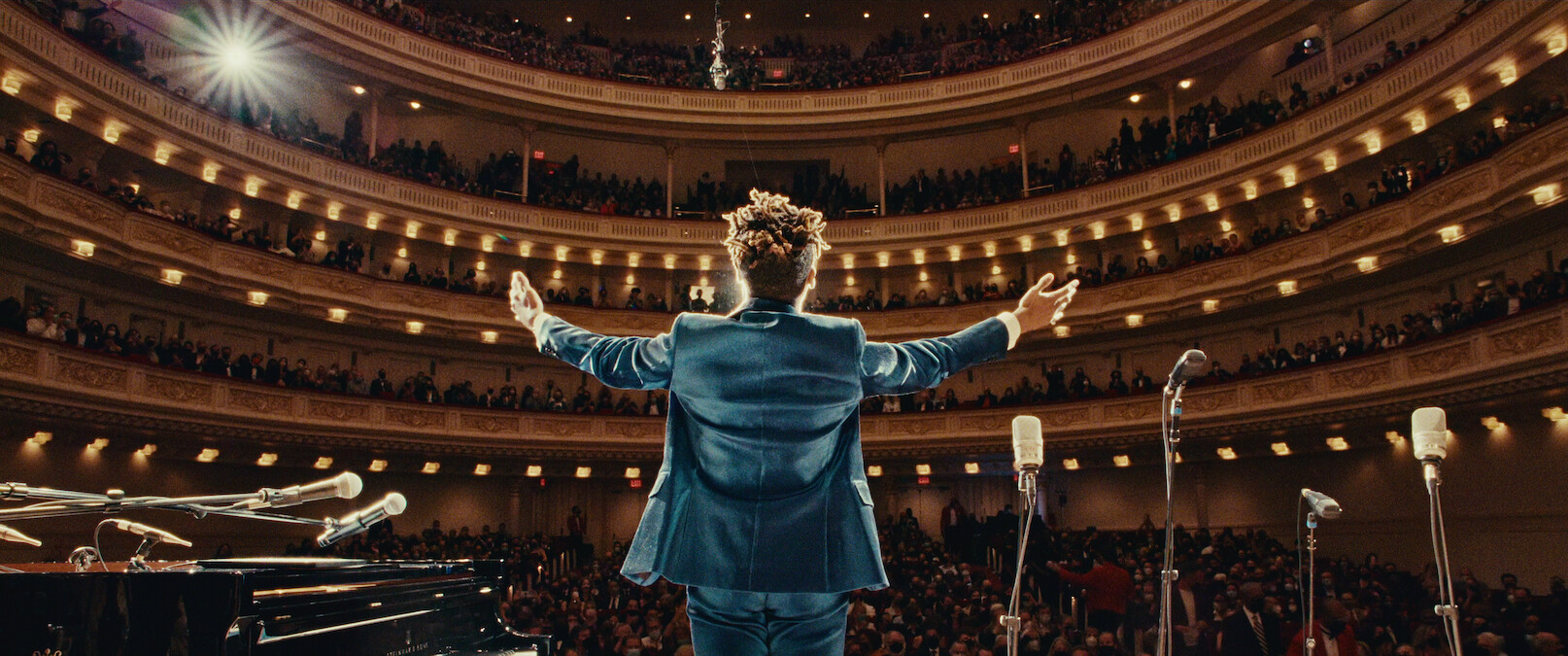 Jon Batiste stands in front of an audience on a stage. 