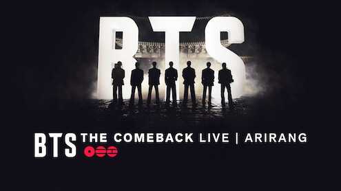 Silhouettes of seven people standing in front of large lit-up BTS letters with "BTS THE COMEBACK LIVE | ARIRANG" text at the bottom, dark concert stage background.
