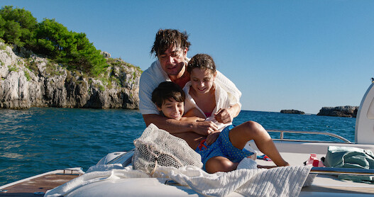 Riccardo Scamarcio as Pietro La Torre embraces two children on the back of a boat in 'Vanished into the Night'