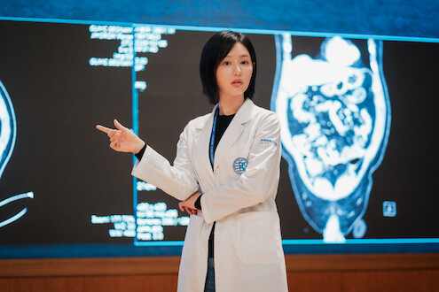 Uma mulher sul-coreana veste jaleco branco e aponta para uma projeção médica na tela