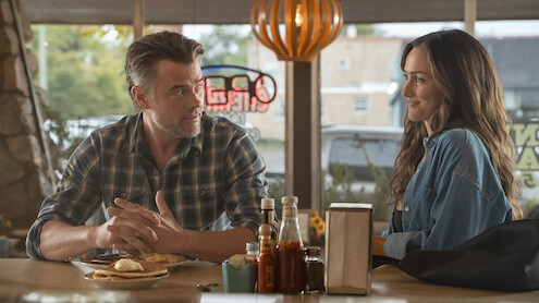  Josh Duhamel as Staten and Minka Kelly as Quinn sit across from each other at a diner table, talking and smiling. Sunlight streams through the windows, and condiments, plates of food, napkins, and a neon sign are visible in a cozy restaurant.