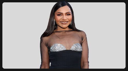 Woman wearing a black dress with sheer top and sparkling embellishments, standing in front of a light gray background, smiling and posing for the camera, formal event setting.