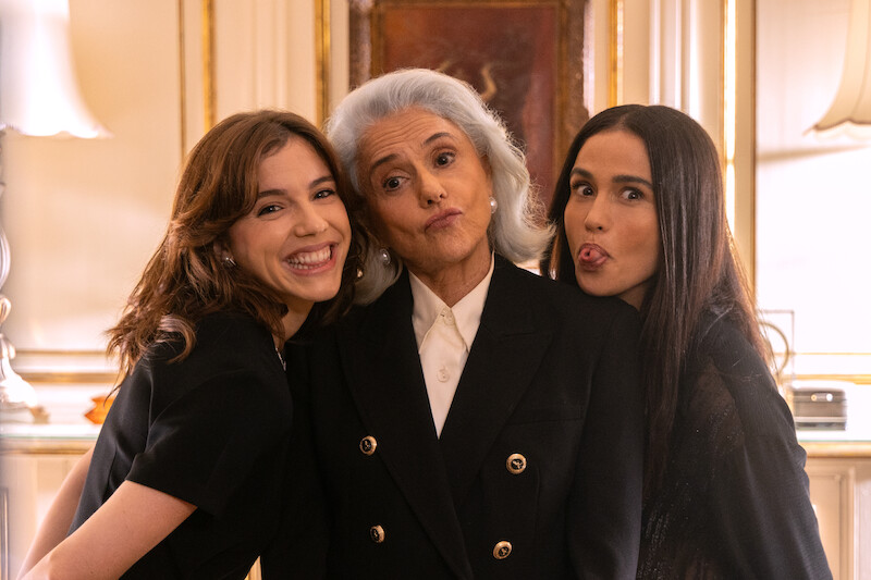 Três atrizes, Marieta Severo (branca, de cabelos grisalhos e vestindo terno preto sonbre camisa branca), Alice Wegmann (de cabelos curtos e castanhos, na altura do ombro, vestindo um vestido preto) e Nanda Costta (de cabelos longos e escuros, vestindo vestido preto) posam lado a lado em uma sala branca com adornos nas paredes