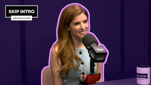 Anna Kendrick, smiling in front of a microphone labeled "SKIP INTRO." She wears a sleeveless, light blue top. The background is deep purple with a purple outline around her.