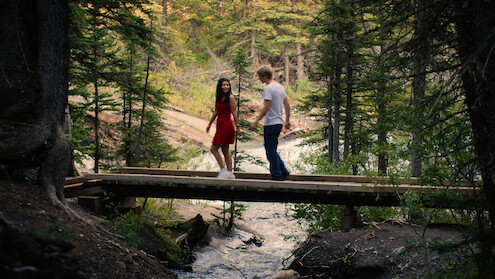 Jackie and Cole walk across a bridge in a forest