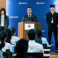 A group of four people face a group of reporters at a press conference.