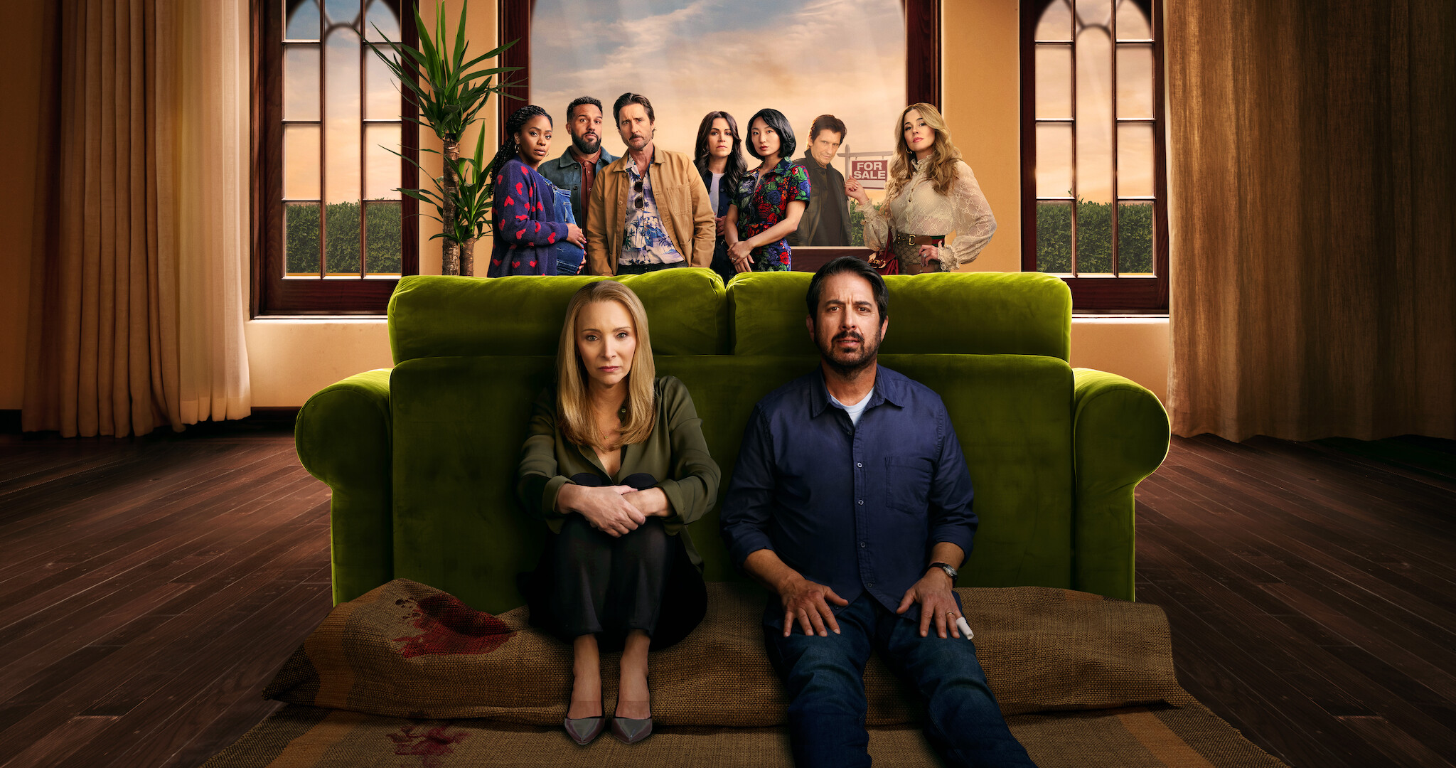 Lisa Kudrow and Ray Ramano hiding behind a couch with other members behind them.