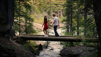 Jackie and Cole walk across a bridge in a forest