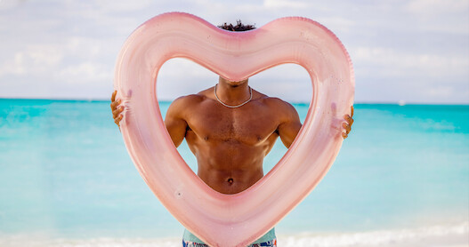 Man without a shirt holding a heart shaped balloon showing off his abs.