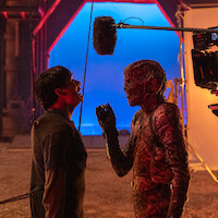 Ator com maquiagem de monstro encara outro ator em um set de filmagem, criando uma atmosfera intensa de bastidores.