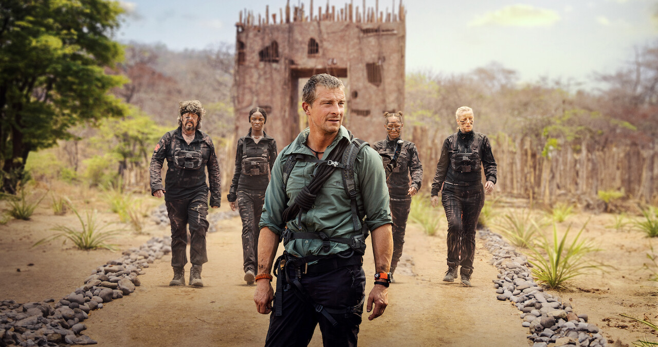 Bear Grylls stands in front of four people on a rocky path. 
