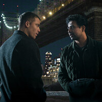Two men talking under a lit bridge at night with city skyscrapers in the background, urban environment, dramatic and serious atmosphere.