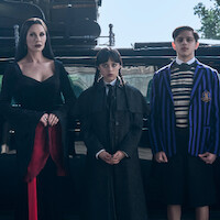 Catherine Zeta-Jones as Morticia Addams, Jenna Ortega as Wednesday, and Isaac Ordonez aș Pugsley Addams stand in front of their car in Season 2 of ‘Wednesday’