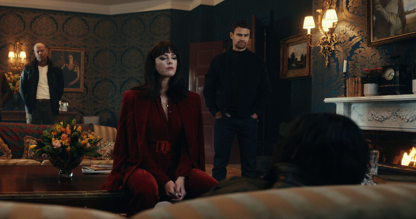 Kaya Scodelario as Susie Glass and Theo James as Eddie Horniman question someone seated on a couch in an ornate room in season 1 of 'The Gentlemen'