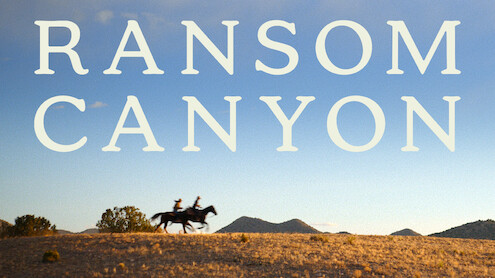 Duas pessoas montadas a cavalo atravessam uma colina coberta de gramíneas sob um céu azul-claro. As palavras ‘Ransom Canyon’ se destacam em letras grandes que ocupam a parte superior da imagem.