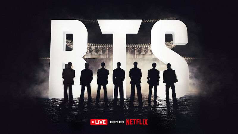 BTS standing silhouetted against giant 'BTS' letters