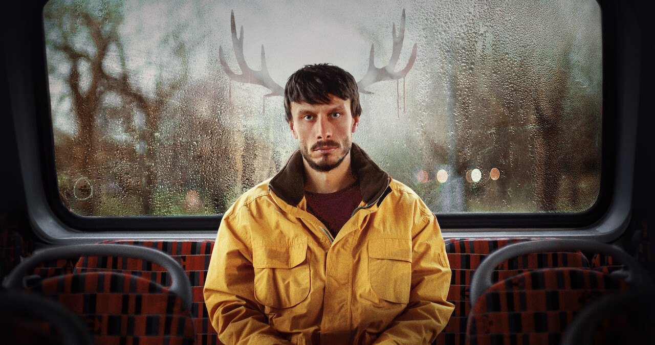 Richard Gadd as Donny Dunn sits in the back of a bus with reindeer antlers outside, behind his head in Season 1 of 'Baby Reindeer'