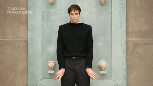 Jacob Elordi stands in front of a blue door while dressed in black.