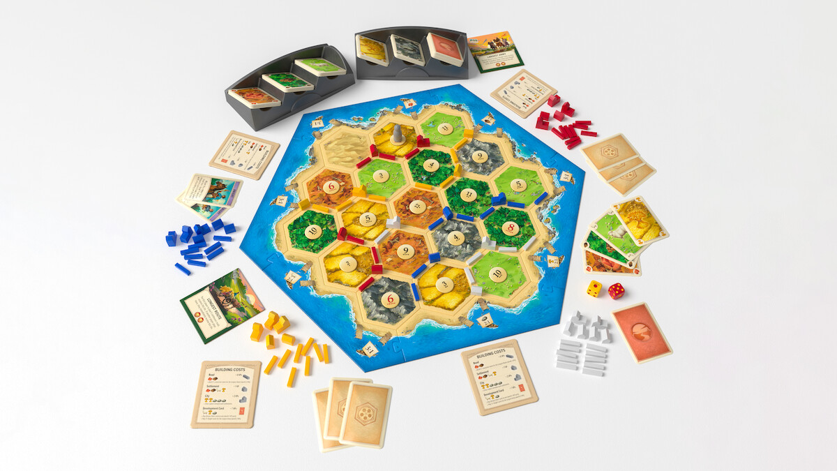 Settlers of Catan board game setup on a white surface, with colorful resource cards, player tokens, dice, and development cards arranged for four players, creating a strategic and inviting gaming atmosphere.