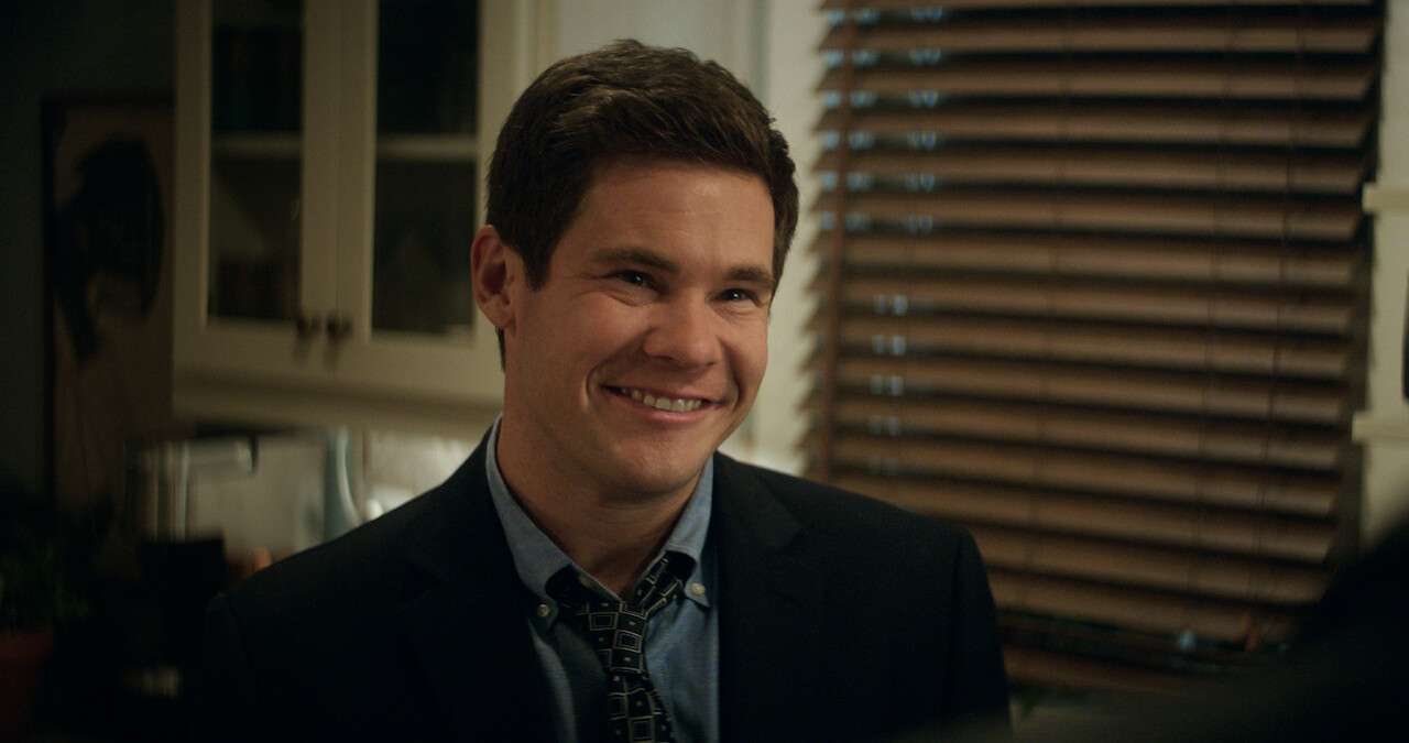 Adam Devine smiles in a kitchen in a still from 'The Out-Laws.'