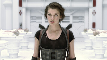 A woman in tactical gear stands in a futuristic, sterile laboratory with white walls and equipment, surrounded by examination tables holding covered bodies, suggesting a sci-fi or action setting.
