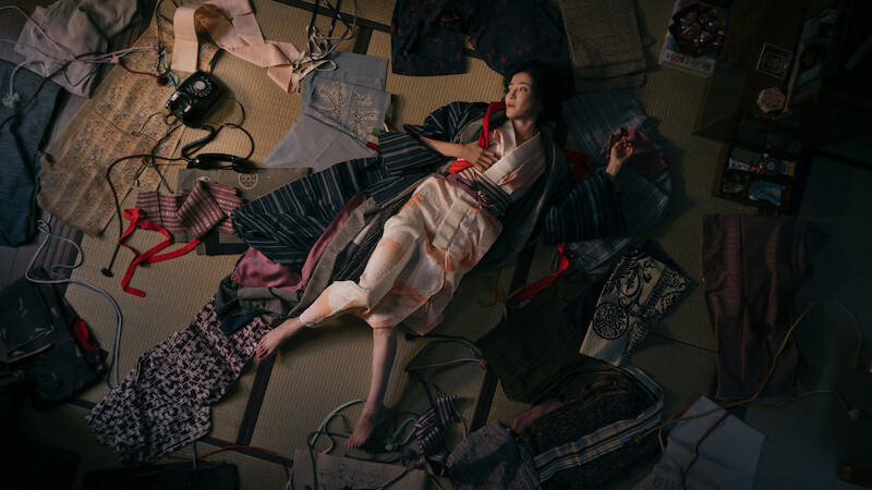 A still image from 'Asura' depicts a woman on the ground surrounded by clothes. 