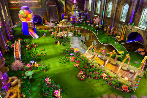 Recriação da fábrica de chocolates de Willy Wonka tem chocolates e flores ao redor de uma passarela coberta por arcos, com um grande 'W' no centro do primeiro arco