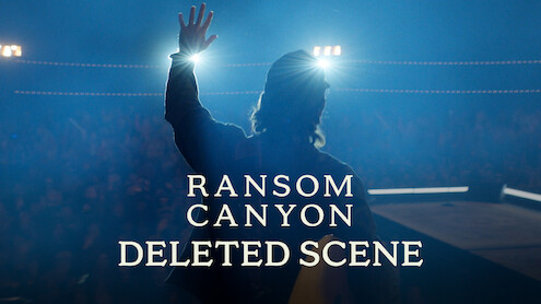 Thomas Rhett stands on stage in silhouette, facing bright spotlights with one hand raised. Smoky blue lighting fills the scene, the audience is barely visible in the background, and a text overlay reads: "Ransom Canyon Deleted Scene."