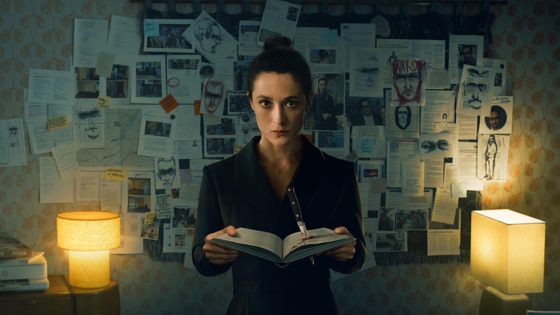 Woman standing in dimly lit room holding an open book, facing the camera, with a wall behind her covered in investigation notes, photos, and sketches, flanked by two glowing lamps.