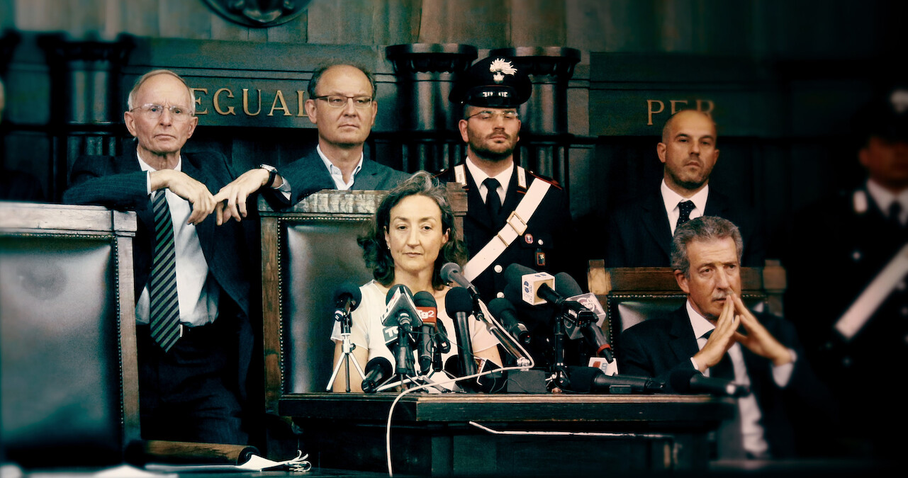 A woman sits in front of a podium with several microphones in 'The Yara Gambirasio Case: Beyond Reasonable Doubt'