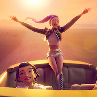 Two animated young women in a convertible at sunset, one standing joyfully with arms outstretched, the other smiling while seated, driving through a desert landscape with warm, golden sunlight illuminating the scene.